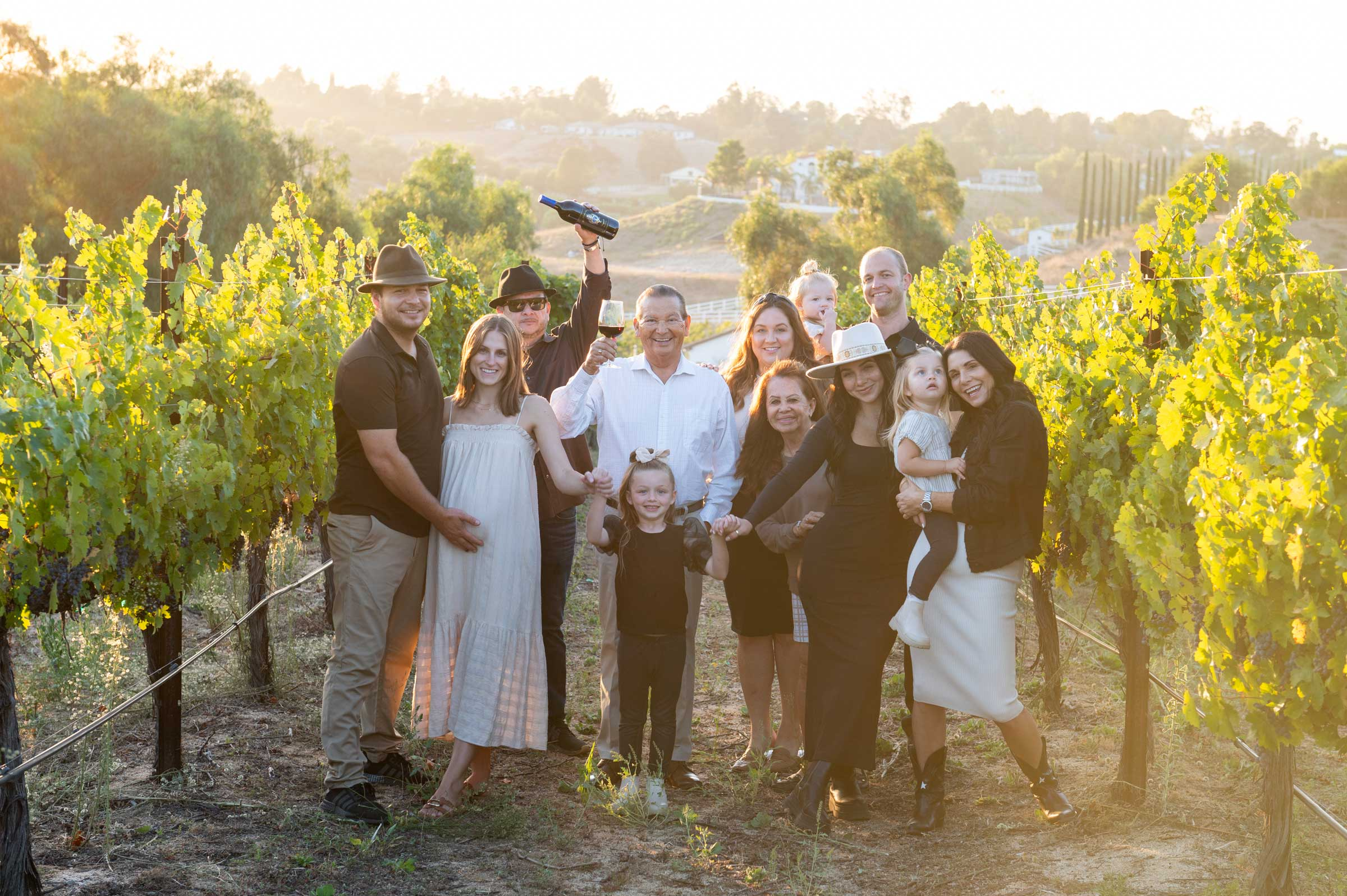 Navarro family standing in vineyards posing for a picture, Rafael ii and iii holding wine bottle and glass.